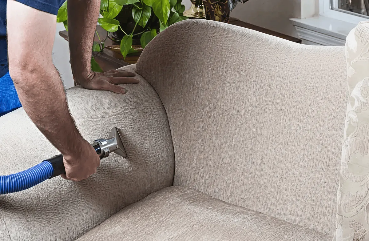 Professional upholstery cleaner deep-cleaning a fabric sofa with a handheld extraction tool and hose, Fort Lauderdale, FL.